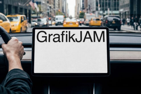 Tablet showing GrafikJAM text held up in NYC taxi with yellow cabs visible