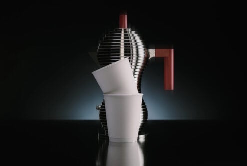 White cups arranged with chrome coffee maker, burgundy handle on dark backdrop