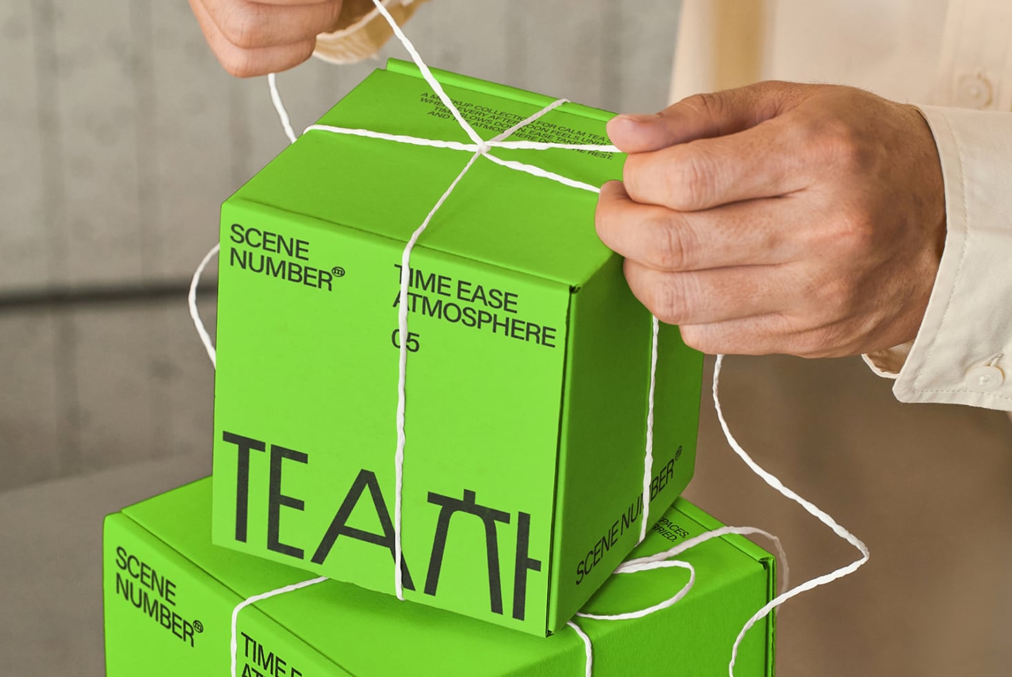 Person holding stacked bright green boxes with white string, product branding on sides visible