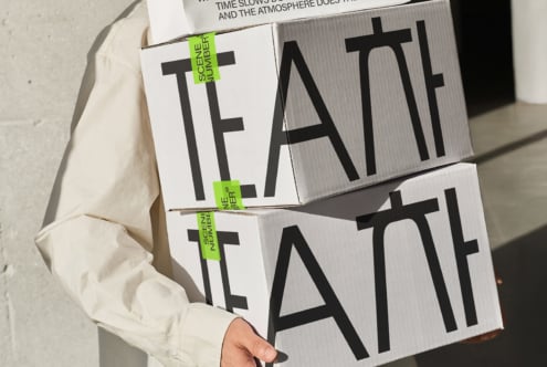 Hands holding stacked white cardboard boxes with TEATT text cutouts
