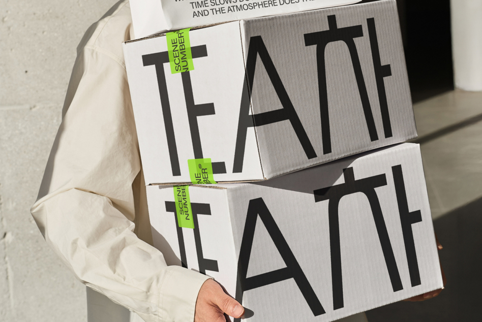 Hands holding stacked white cardboard boxes with TEATT text cutouts