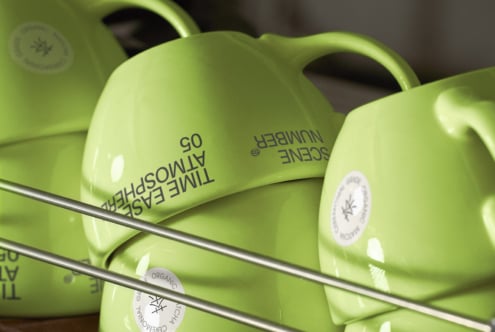 Lime green ceramic mugs arranged on shelf with curved handle detail visible