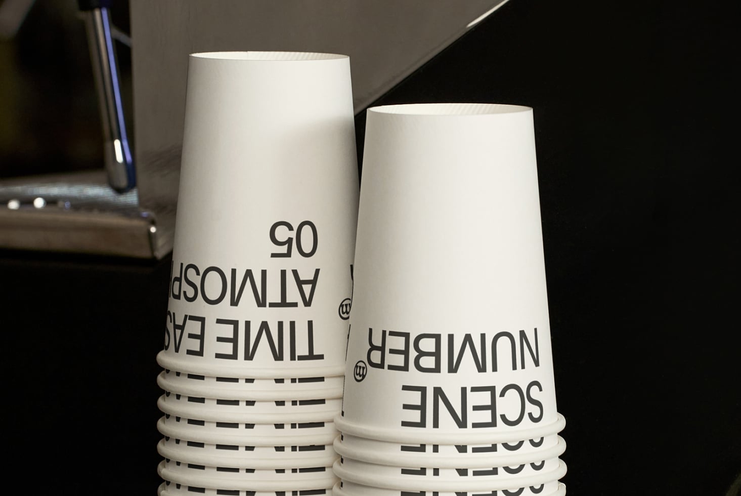 Stack of white paper cups with black dashed bands on dark metallic surface