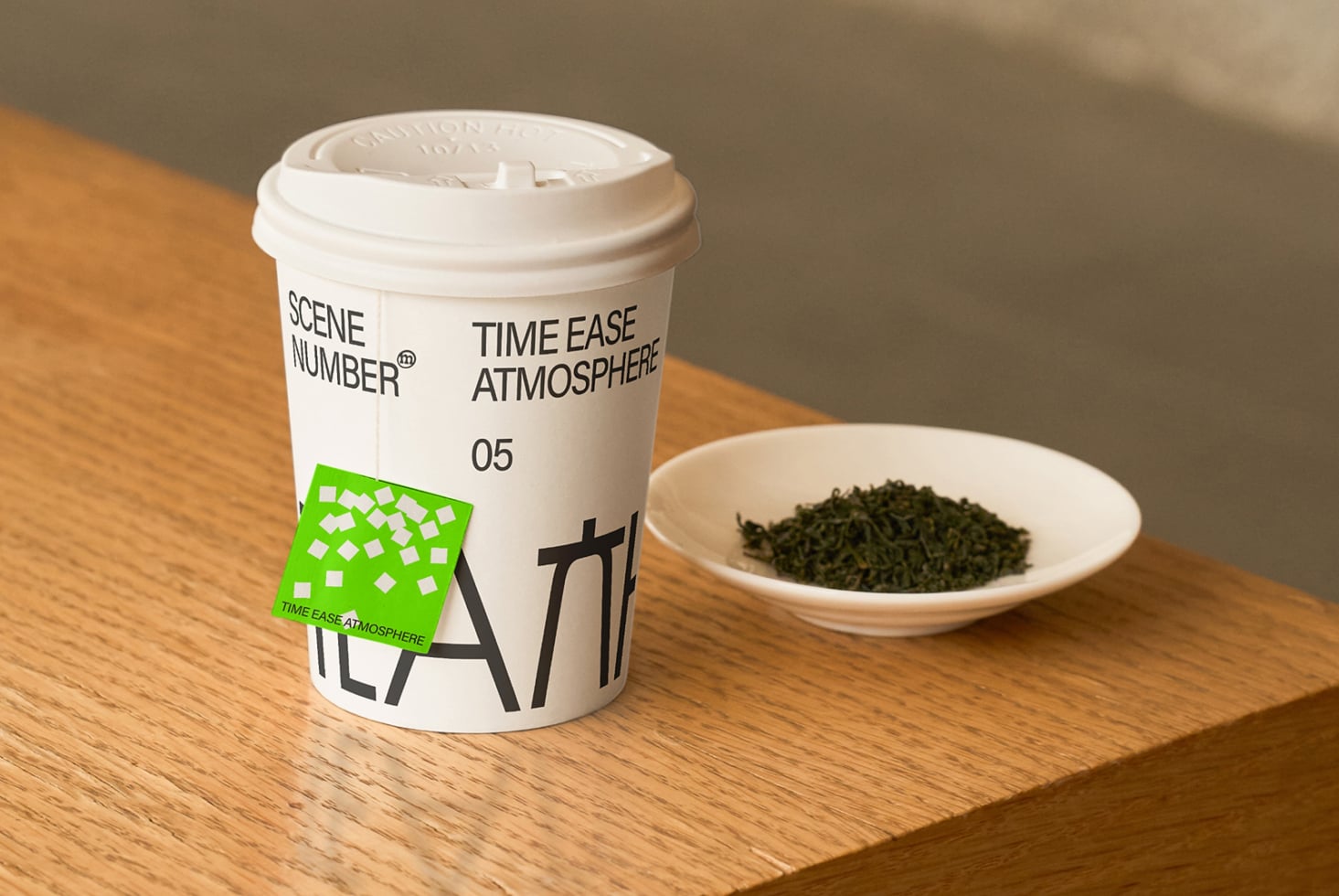 White coffee cup mockup with green label next to ceramic bowl of dried herbs on wood