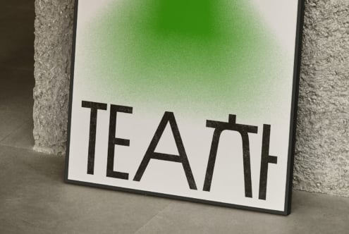 White poster with green gradient displaying TEAL text leaning against concrete wall