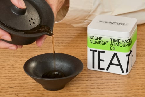 Liquid pouring into dark bowl beside bright green tea canister