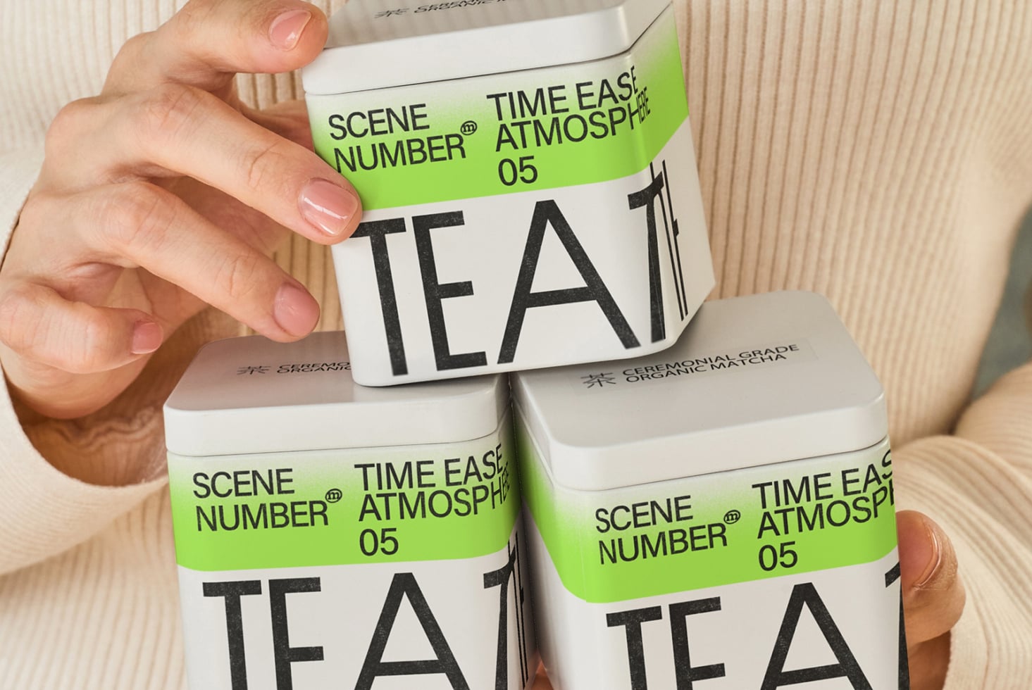 Hand holding lime green tea canister stacked with two white boxes
