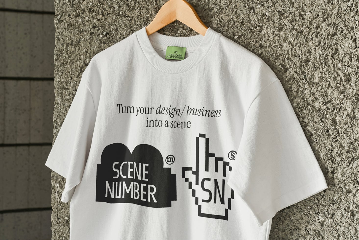 White tee with Scene Number branding on wooden hanger against concrete wall