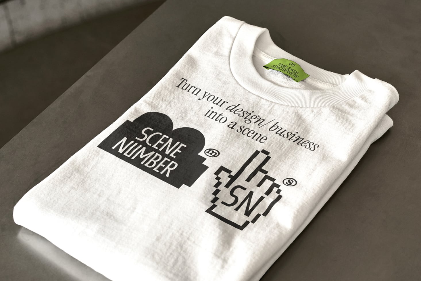 Cream colored t-shirt folded with Scene Number tea design on gray surface