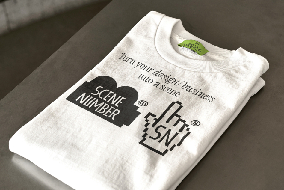 Cream colored t-shirt folded with Scene Number tea design on gray surface