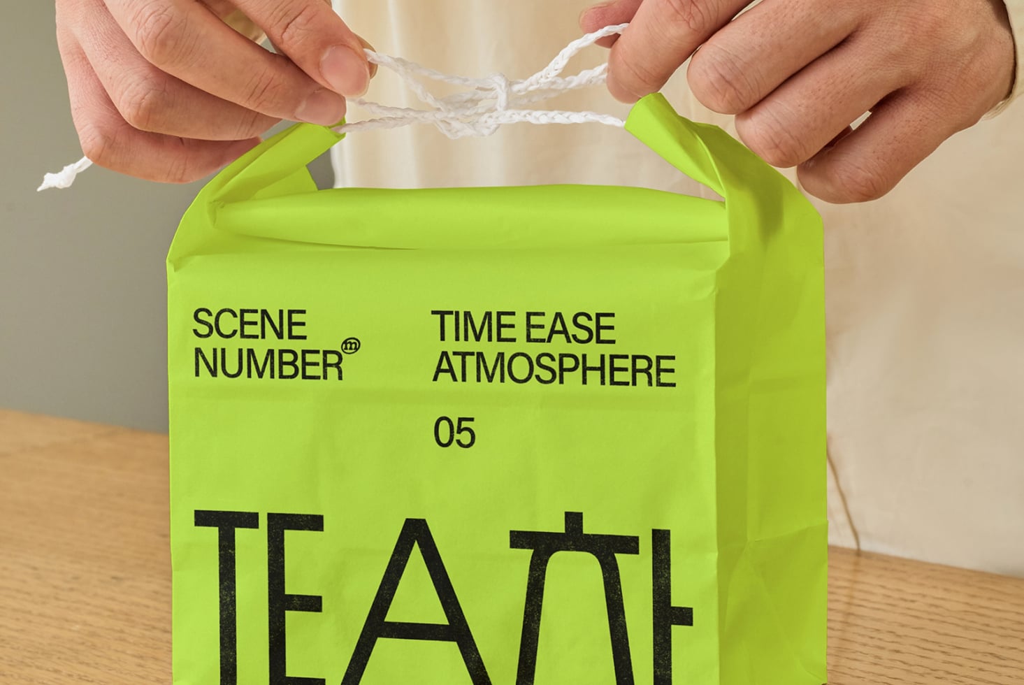 Hands holding neon green paper bag with twine handles showing printed branding