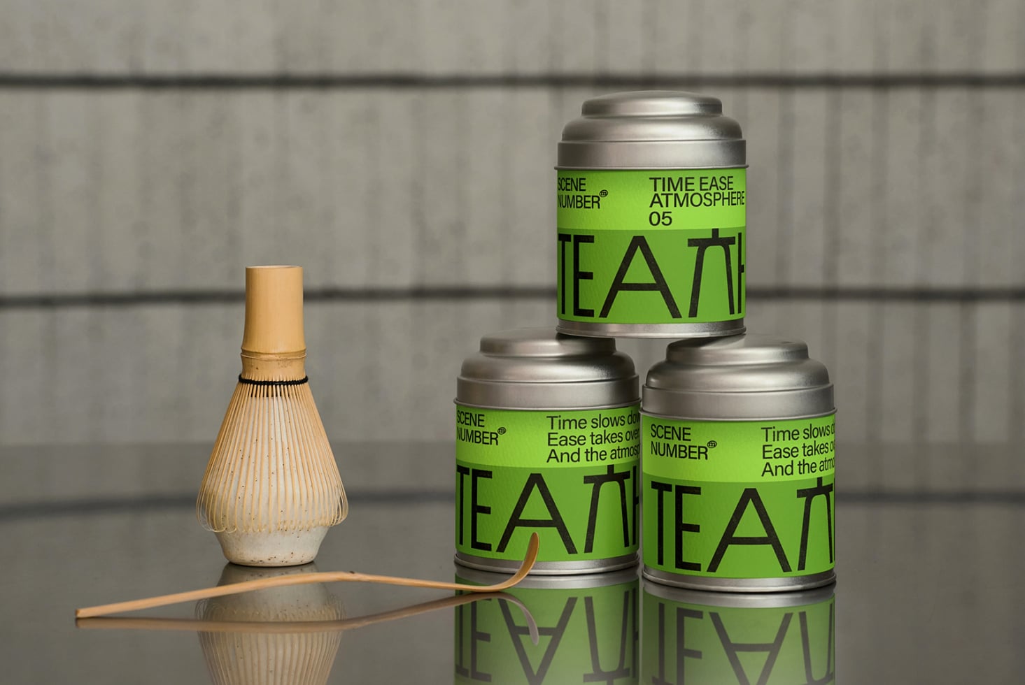 Three metal tea canisters stacked with matcha whisk on concrete backdrop