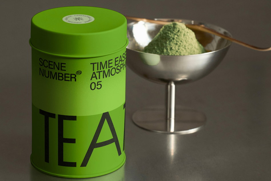 Bright green tea tin with matcha whisk beside silver bowl filled with green powder