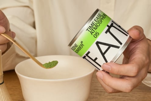 Hand pouring green matcha powder from branded tin into ceramic bowl