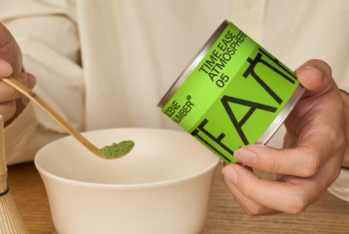 Hand pouring green matcha powder from bright canister into bowl
