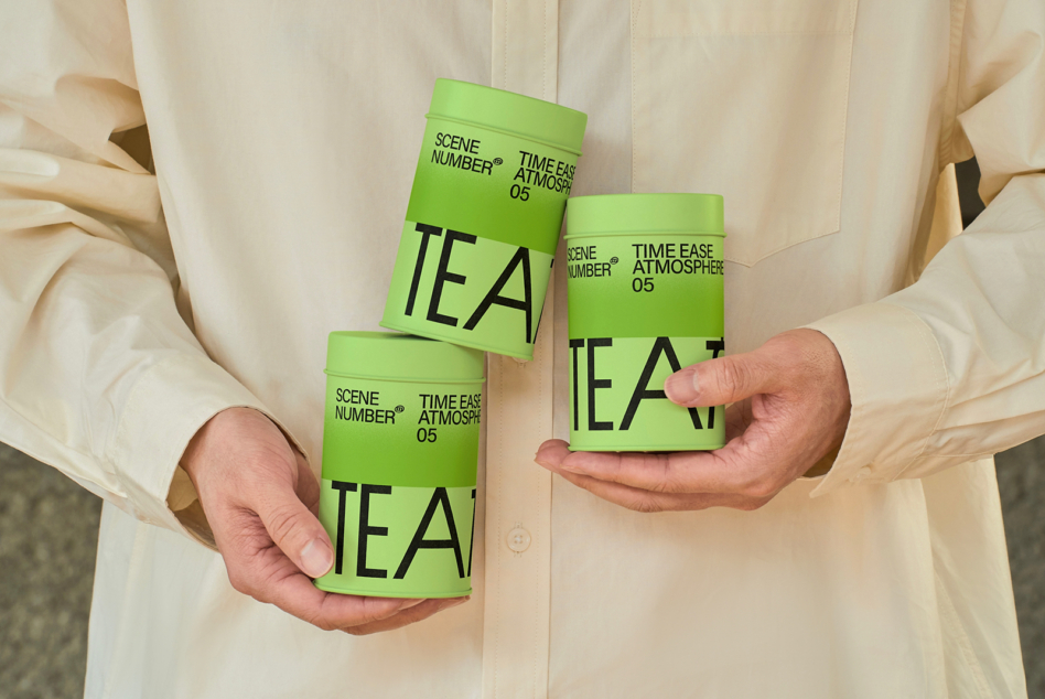 Three canisters with green lower half, white upper half, held in hands, TEA design