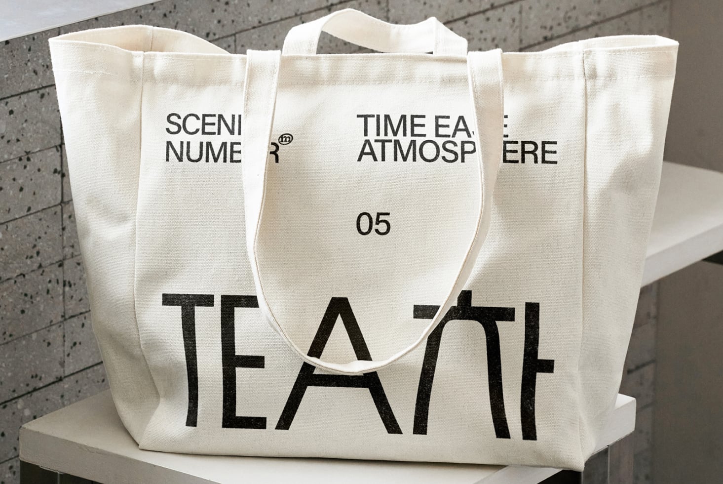 Natural canvas tote with bold black TEA text, displayed on platform, front view