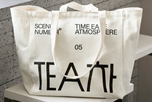 Natural canvas tote with bold black TEA text, displayed on platform, front view