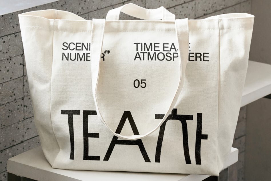 Natural canvas tote with bold black TEA text, displayed on platform, front view