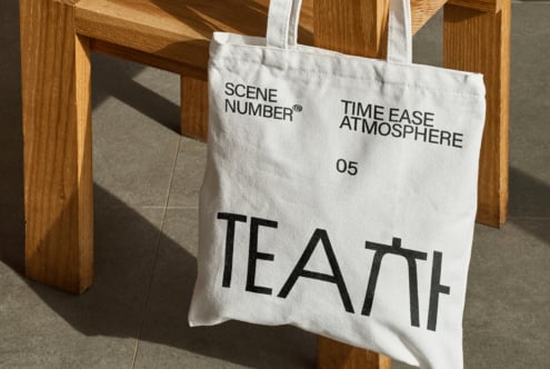 Off white canvas tote bag hanging on wooden chair with large TEA lettering