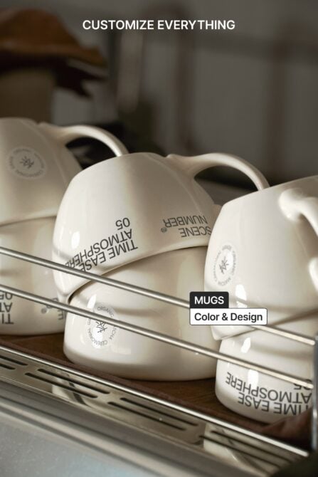 White ceramic mugs with printed logo on metal shelf with soft shadows