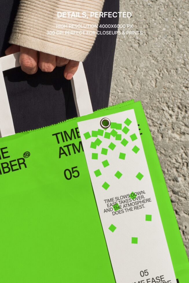 Close up of hands holding white paper bag with lime green tag, concrete wall backdrop