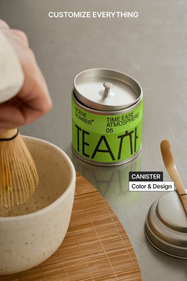 Green tea canister with metal lid surrounded by matcha whisk on wood