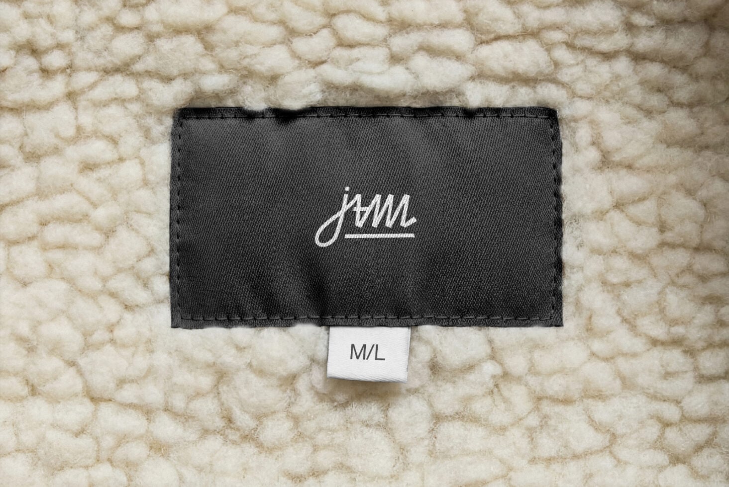 White cursive JAM logo on black label lying flat on cream chunky knit