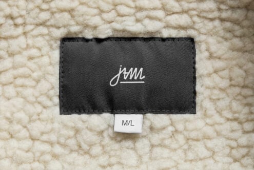 White cursive JAM logo on black label lying flat on cream chunky knit