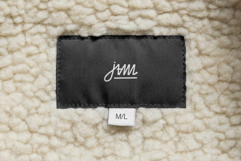 White cursive JAM logo on black label lying flat on cream chunky knit