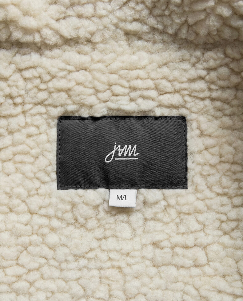 Black label with white cursive JAM logo on cream knit fabric, M/L size tag below