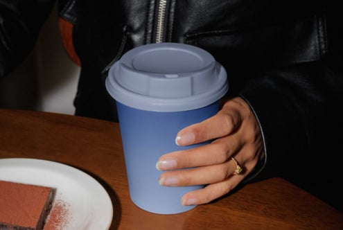 Periwinkle blue coffee cup with white lid in person's grip