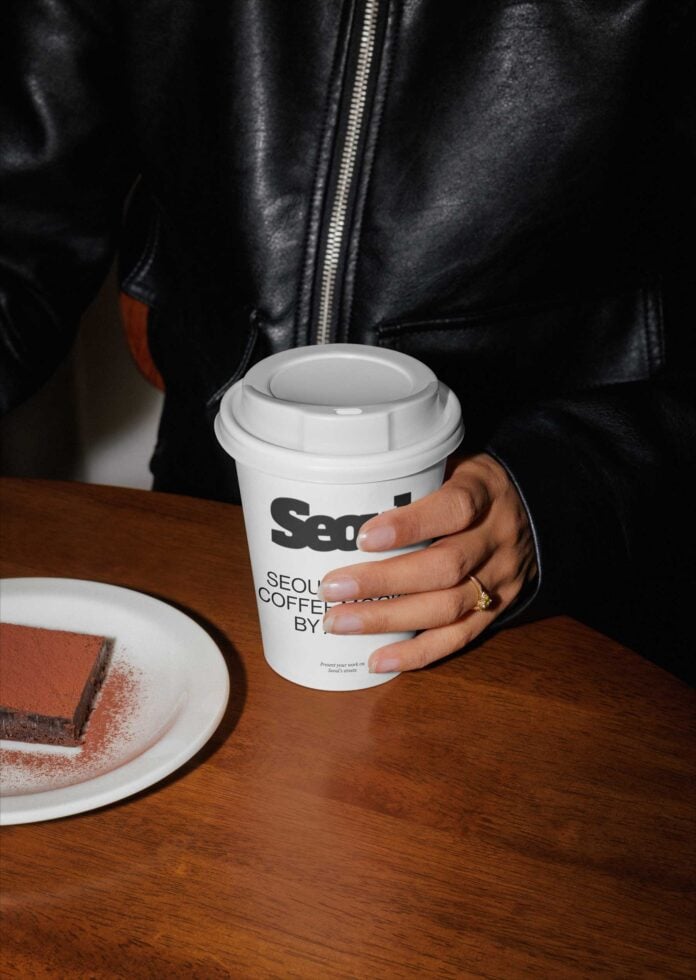 White coffee cup with branding held in hand over wooden table