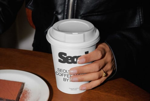 White takeaway cup with logo mockup held by model indoors