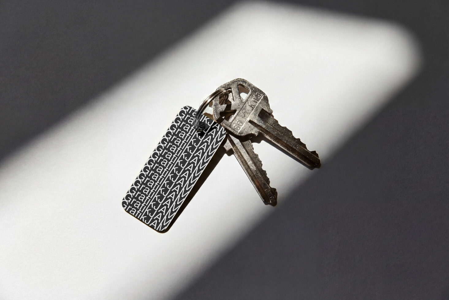 Metal key with repeating jWML text engraved on tag casting shadow on white