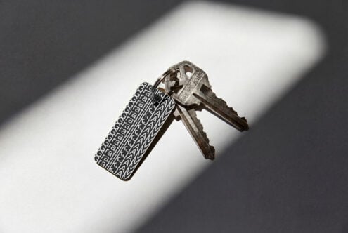 Metal key with repeating jWML text engraved on tag casting shadow on white