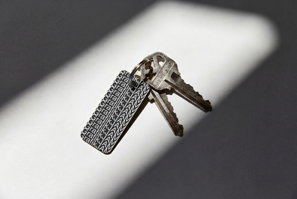 Metal key with repeating jWML text engraved on tag casting shadow on white