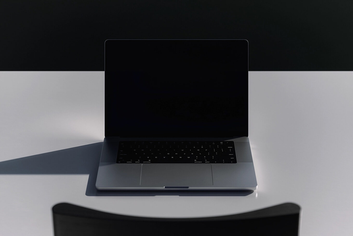 Laptop with black screen open front view on white surface with minimal lighting