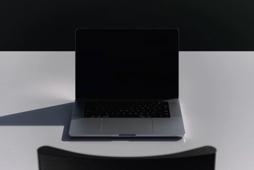 Laptop with black screen open front view on white surface with minimal lighting