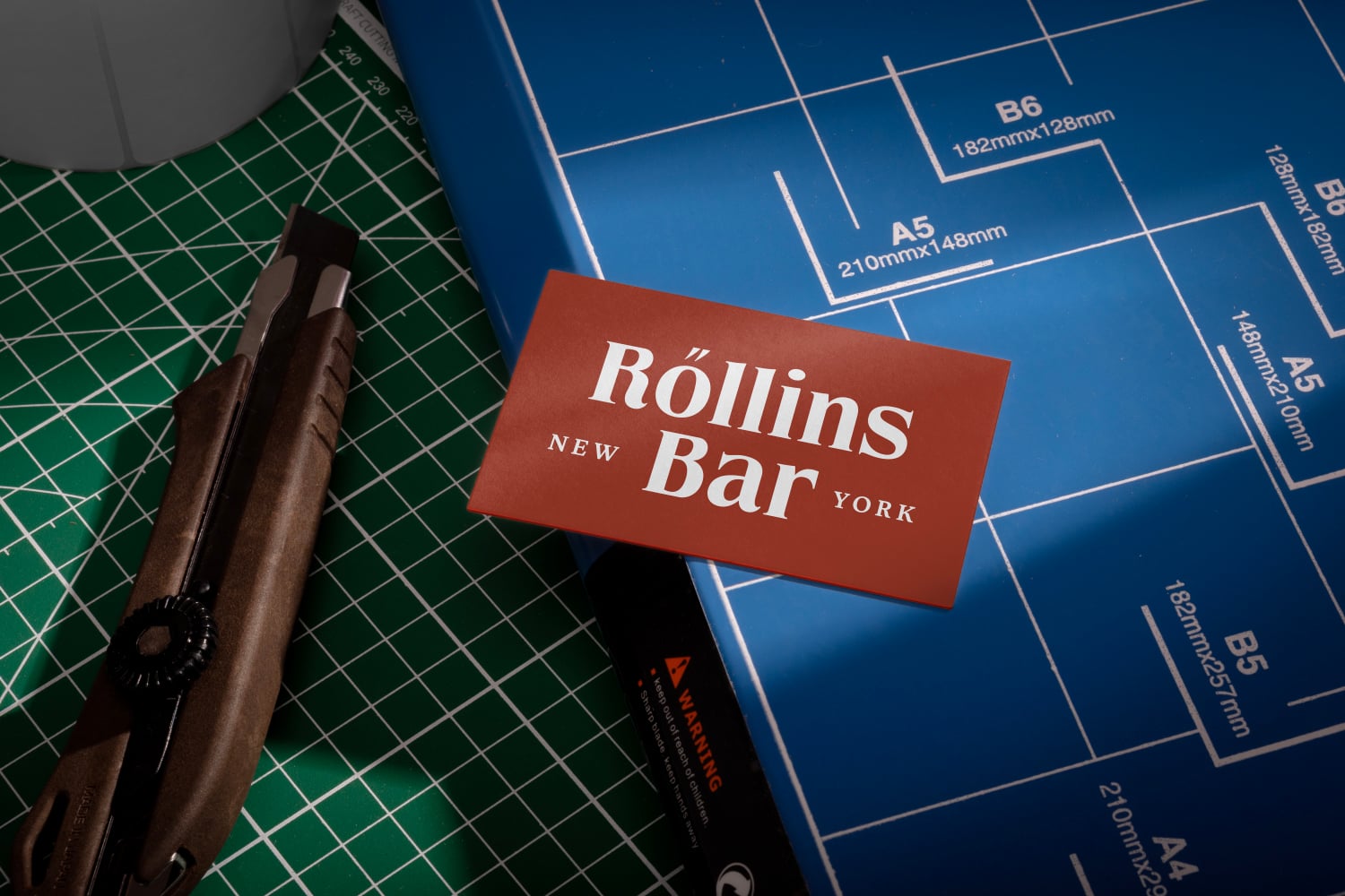 Rust business card for Rollins Bar New York on drafting paper with cutting mat