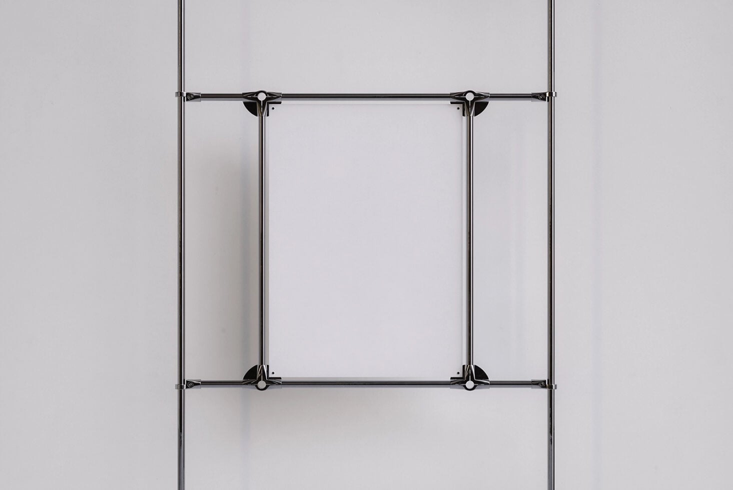 Two vertical metal clamps securing empty poster frame on white surface