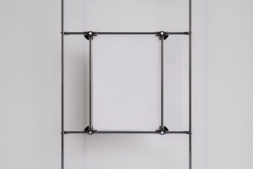 Two vertical metal clamps securing empty poster frame on white surface