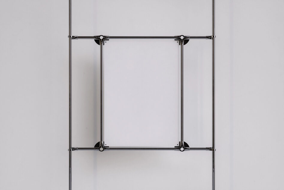 Two vertical metal clamps securing empty poster frame on white surface