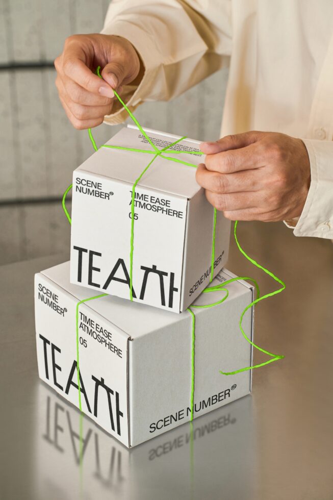 Hands unboxing stacked white tea boxes with neon green string wrapping