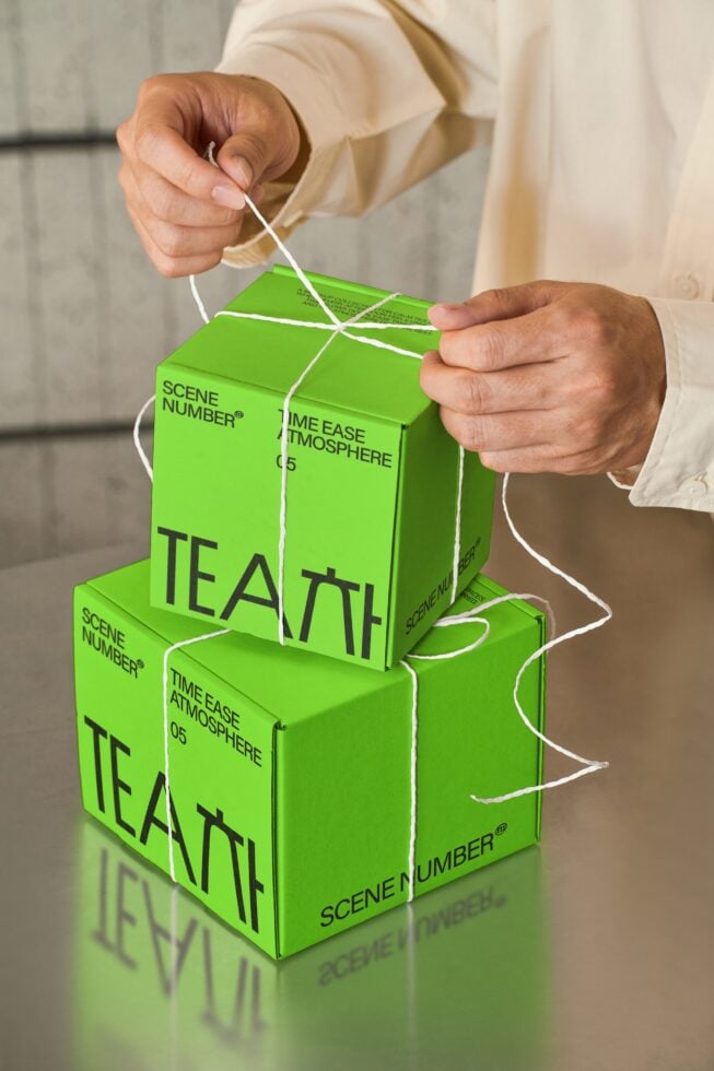 Hands holding stacked bright green tea boxes tied with white string twine