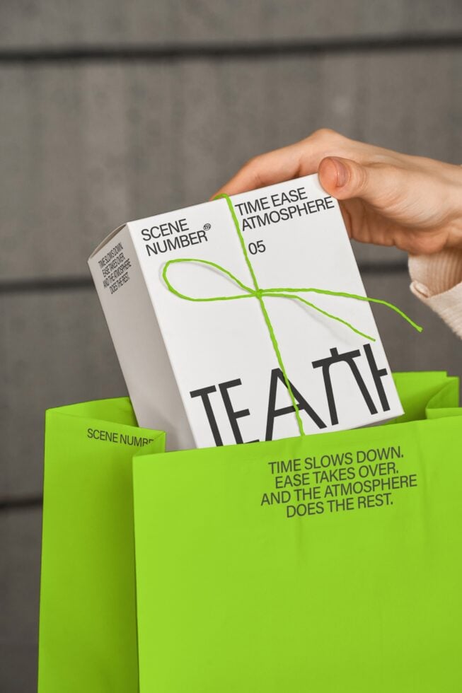 Hand holding open white paper bag with green twine bow revealing tea box inside