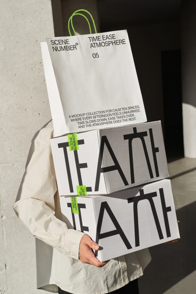 Cream paper shopping bag with green handles layered over grayscale corrugated boxes with tea branding