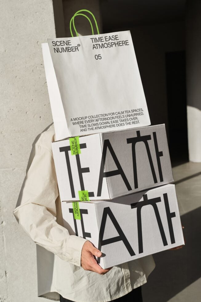 Person holding stacked white boxes with bold black typography, lime green handles, minimal branding mockup
