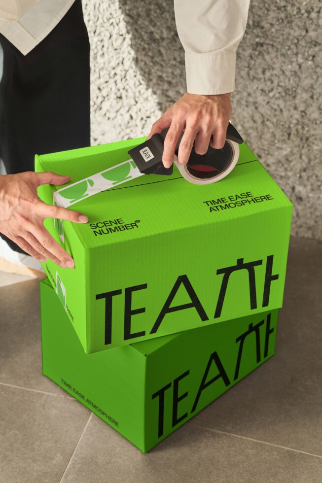 Close up of hands sealing bright green tea box with branded tape on concrete surface