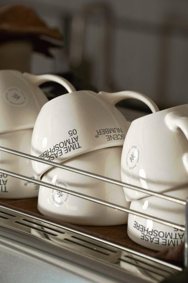 Row of cream white ceramic mugs with circular brand stickers displayed